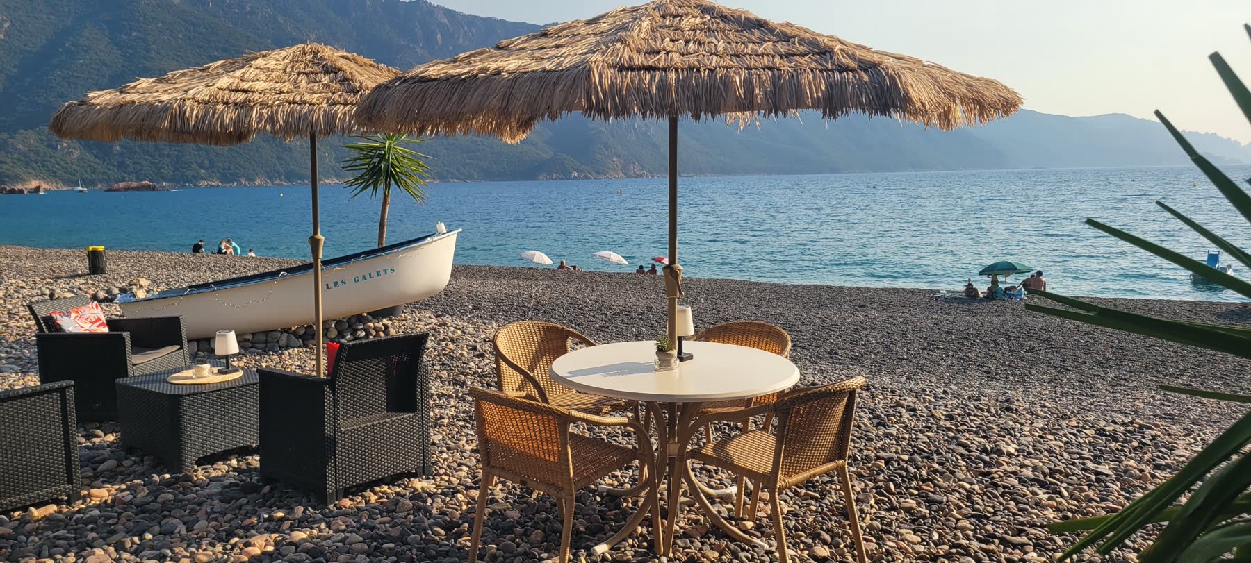 La barque Les Galets amarrée sur la plage, entre les parasols de paille